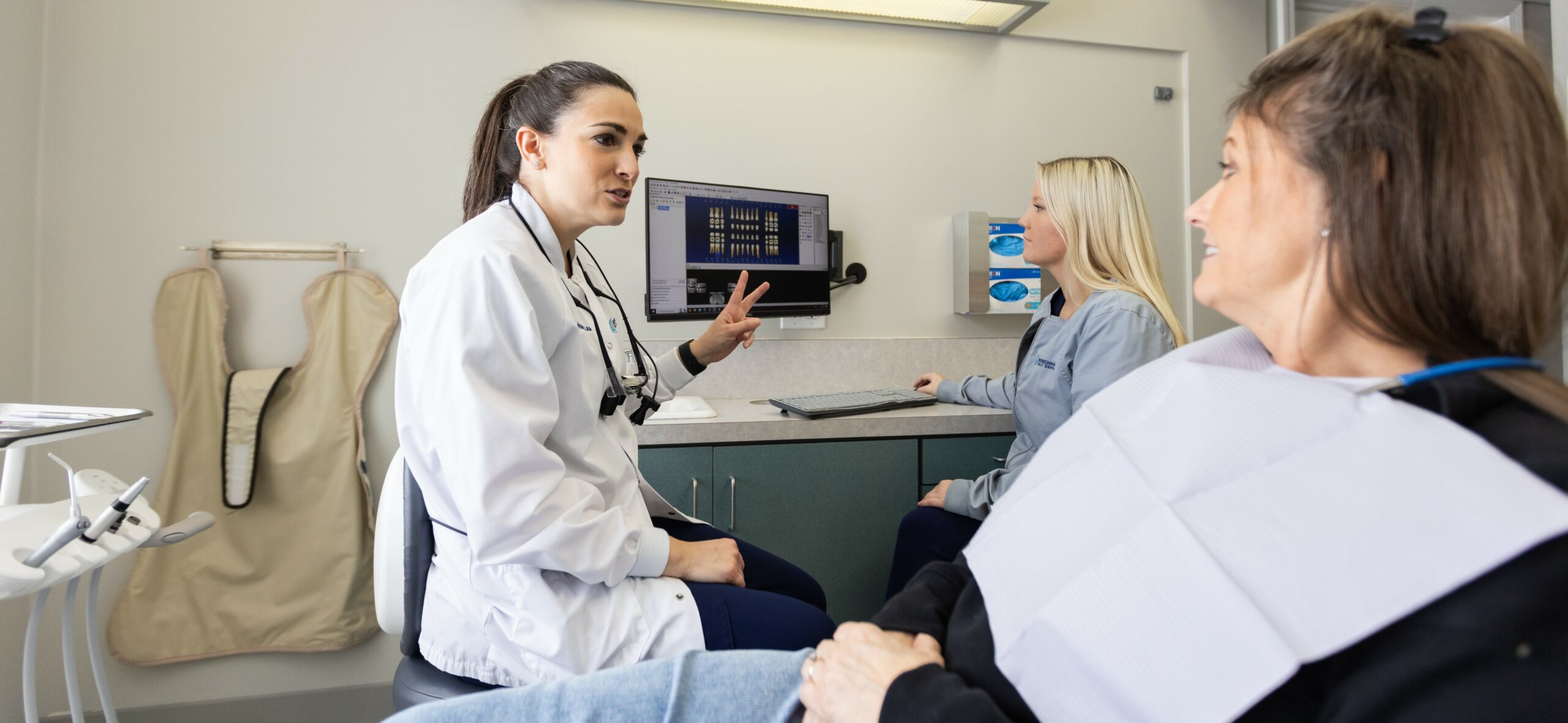 A dentist explaining X-ray results to a female patient with the assistant seated nearby